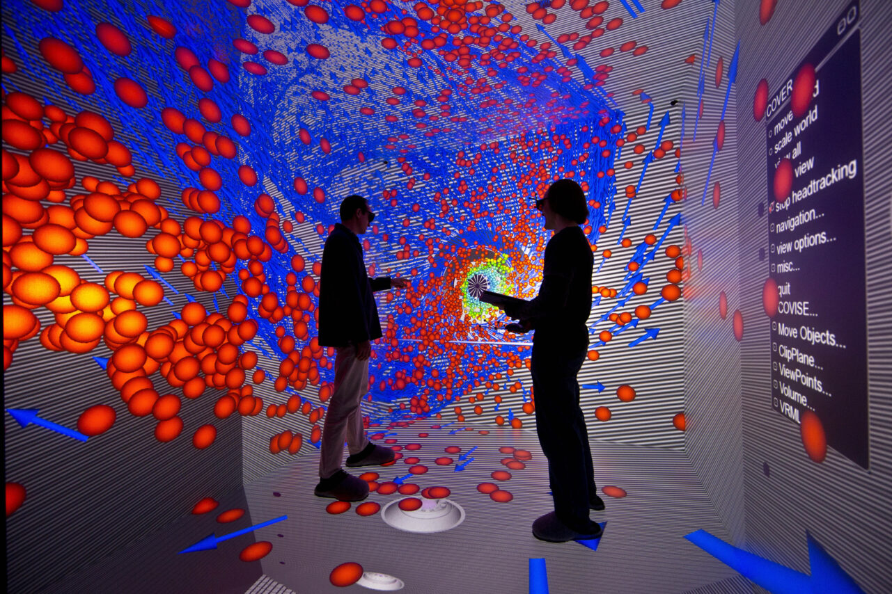 Two individuals wearing 3D glasses stand in an immersive virtual reality environment filled with a 3D projection of orange spheres and blue arrows, creating a tunnel-like effect. They are interacting with the visualization using handheld devices. A menu with options such as "move," "scale world," and "navigation" is visible on the right side, indicating a control interface for the virtual environment. The scene is vibrant and dynamic, focusing on data visualization.